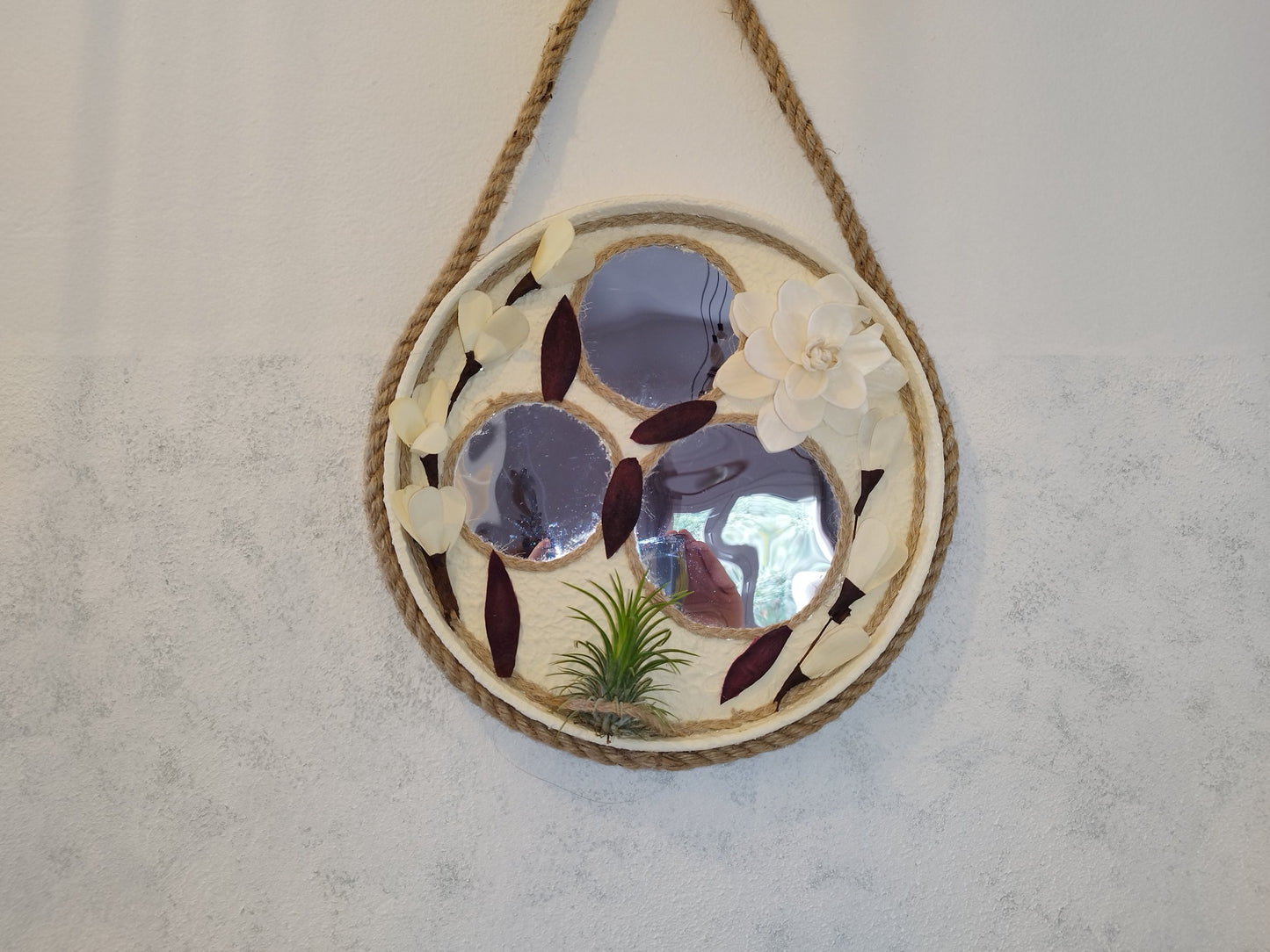 Decorative wall mirror with floral design and rope hanging on a plain wall