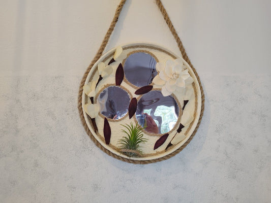 Decorative wall mirror with floral design and rope hanging on a plain wall
