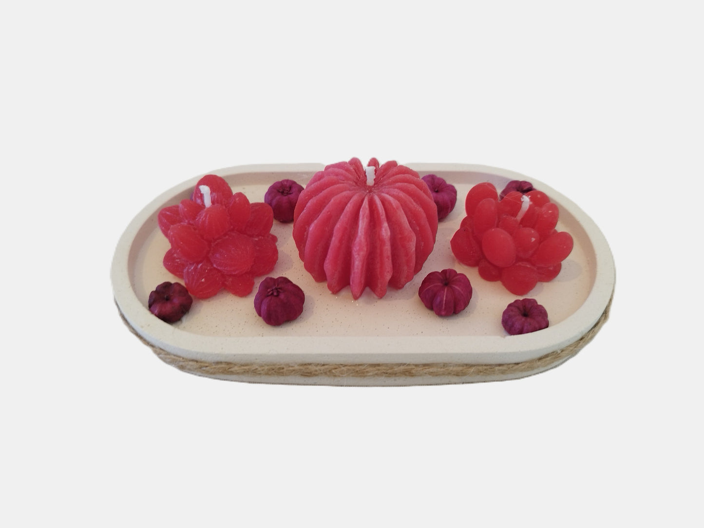 Set of red floral and berry-shaped candles on a white cement plate with a white background