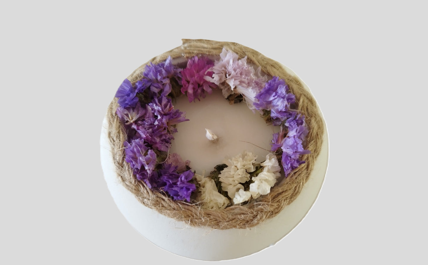 Κερί σόγιας σε λευκό τσιμεντένιο δοχείο με στεφάνι από μωβ και ροζ λουλούδια σε γκρι φόντο απο την επανω πλευρά