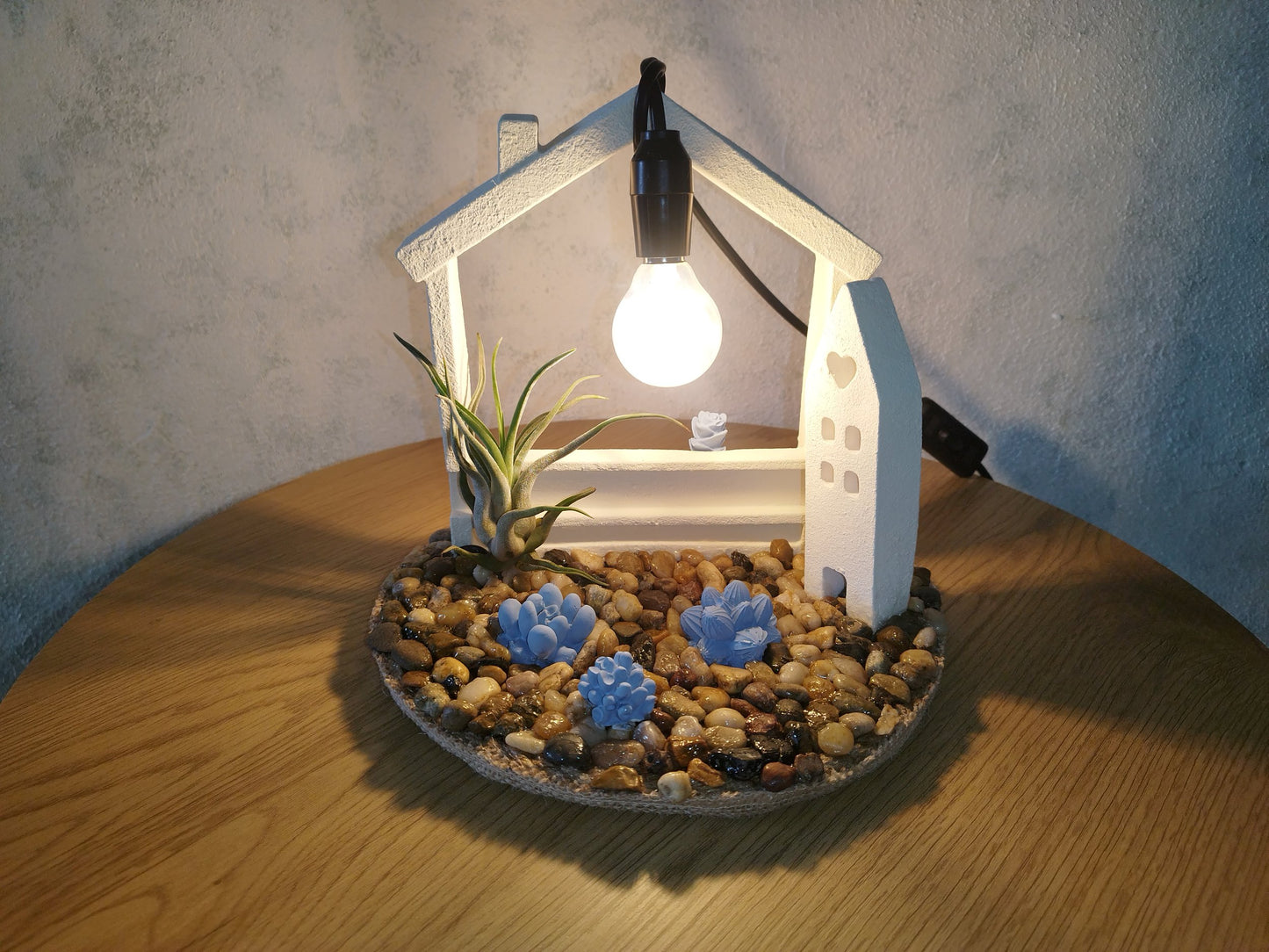 Decorative lamp shaped like a house with plants and rocks on a wooden table