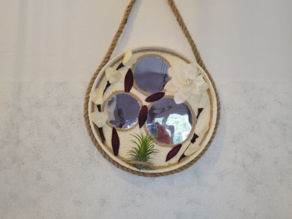 Decorative wall mirror with floral design and rope hanging on a plain wall