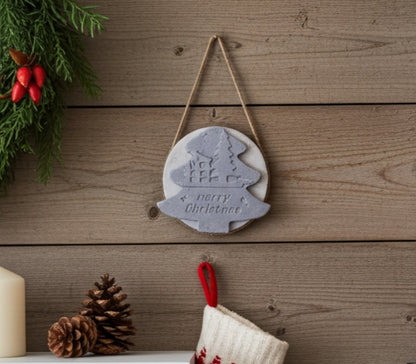 Decorative Christmas ornament with tree design and 'Merry Christmas' text, hanging on a wooden wall.