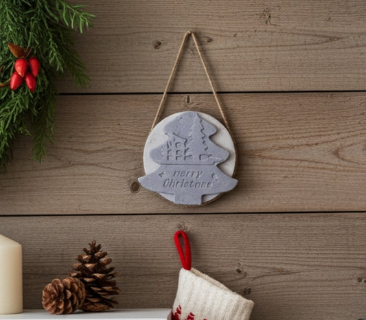 Decorative Christmas ornament with tree design and 'Merry Christmas' text, hanging on a wooden wall.