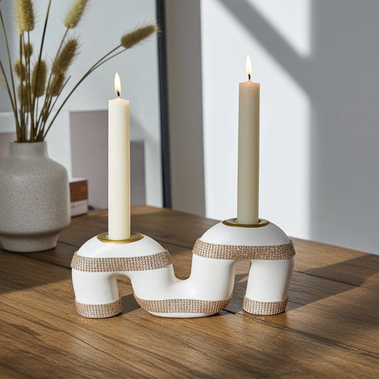 Two white candle holders with gold accents holding lit candles on a wooden surface