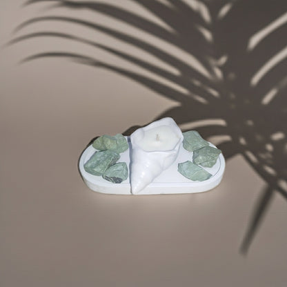 Candle with green stones on a white plate in a grey surface

