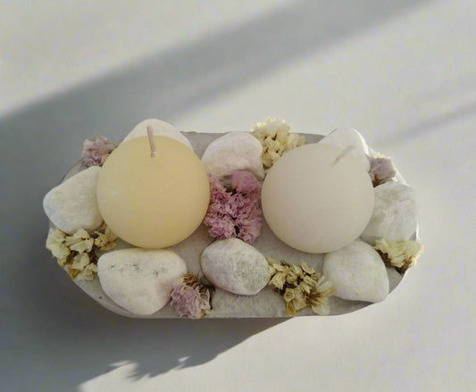 Κεριά πάνω σε τσιμεντένια βάση διακοσμημένα με πέτρες με γκρι σκιές